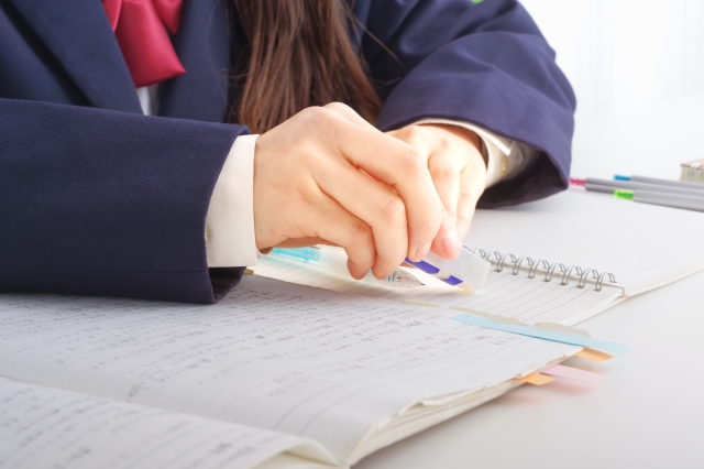 紺のブレザー制服と赤いリボンを着用し、教科書やノートを前に消しゴムで書き直しながら勉強に励む、現役女子高校生の自学自習の様子